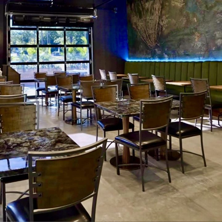 Contemporary dining room at Blake’s Oyster Bar in Atlanta, featuring custom olive green banquette seating, marble-look dining tables, modern metal-framed chairs, botanical wall art, and blue LED accent lighting.
