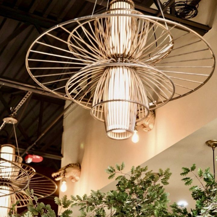 Sculptural industrial-style chandeliers by Currey & Company featuring circular metal frames, complemented by custom-fabricated alligator-head light fixtures holding exposed bulbs in a New Orleans-inspired restaurant.