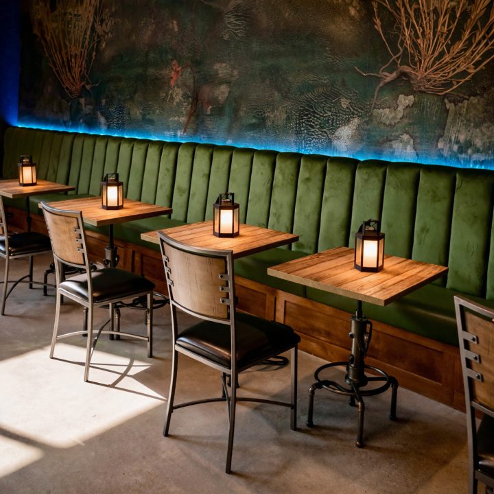 New Orleans-inspired restaurant interior featuring wood-look dining tables with custom industrial metal bases, vintage-style tabletop lanterns, and atmospheric accent lighting.