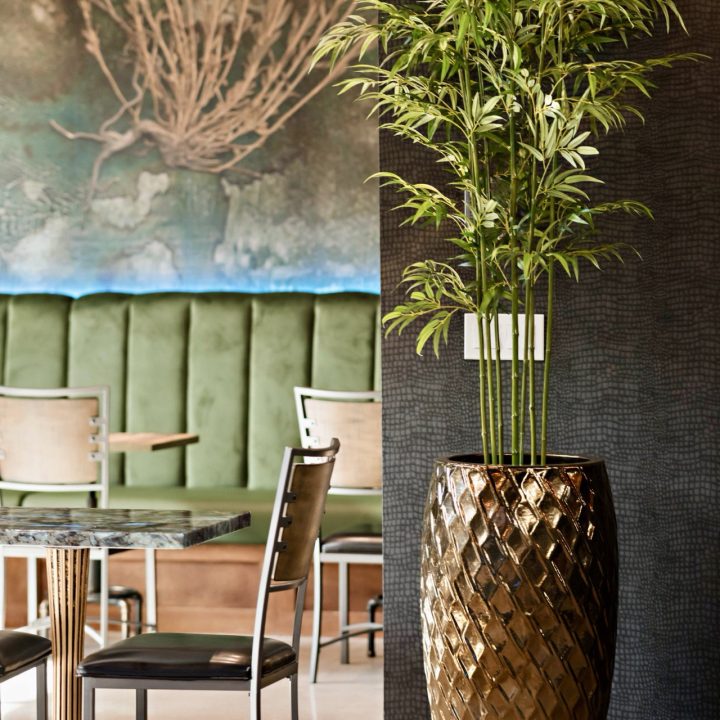 Modern Atlanta restaurant interior featuring olive green velvet banquette seating, aligator textured accent walls, sculptural gold planters, marble-top tables, and contemporary dining furniture designed by Contemporary LUX.